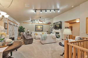 Carpeted living area featuring lofted ceiling, ceiling fan, and a glass covered fireplace