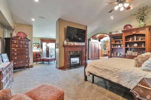 Bedroom with light carpet, arched walkways, a high end fireplace, a textured ceiling, and recessed lighting