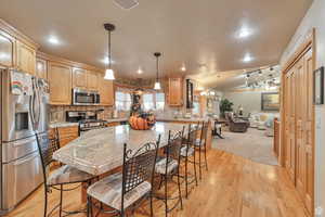 Kitchen with appliances with stainless steel finishes, decorative backsplash, hanging light fixtures, a breakfast bar area, and lofted ceiling