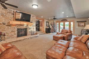 Living area with a ceiling fan, carpet, french doors, a stone fireplace, and a textured ceiling