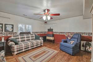 Living room featuring wood finished floors, wainscoting, a textured ceiling, and ceiling fan