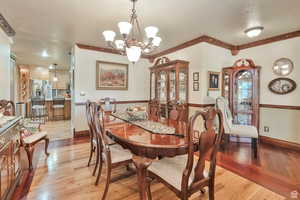 Dining area with light wood finished floors, a chandelier, a textured ceiling, and ornamental molding