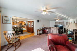 Carpeted living room featuring a ceiling fan, a chandelier, a textured ceiling, and wood finished floors