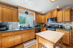 Kitchen featuring stainless steel appliances, wallpapered walls, light wood-style flooring, dark countertops, and recessed lighting
