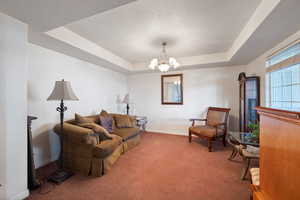 Carpeted living area with a tray ceiling and a chandelier