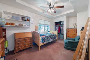 Carpeted bedroom featuring a tray ceiling, a closet, and ceiling fan