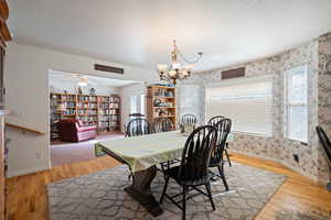 Dining area featuring light wood-type flooring, plenty of natural light, wallpapered walls, a chandelier, and a textured ceiling