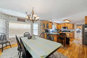 Dining space featuring wallpapered walls, light wood finished floors, a chandelier, washer / clothes dryer, and a textured ceiling