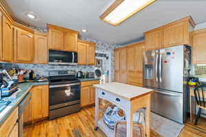 Kitchen with stainless steel appliances, decorative backsplash, light wood-style flooring, washer / clothes dryer, and wallpapered walls