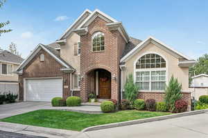 Traditional-style home featuring brick siding, driveway, stucco siding, an attached garage, and roof with shingles
