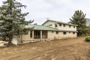 Back of house with covered porch, brick siding, a chimney, a metal roof, and an attached garage