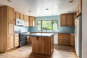 Kitchen featuring white appliances, brown cabinets, a kitchen island, a textured ceiling, and recessed lighting