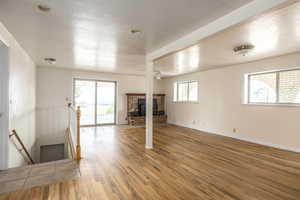 Unfurnished living room with a textured ceiling, light wood finished floors, a brick fireplace, and plenty of natural light