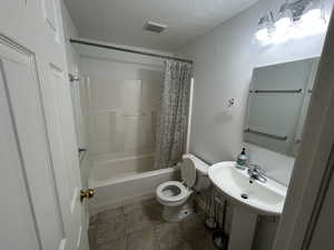 Full bath with shower / bath combo with shower curtain and stone finish floors