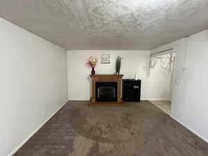 Unfurnished living room featuring a fireplace with raised hearth, dark colored carpet, and a textured ceiling