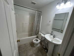 Bathroom with shower / bath combo with shower curtain and stone finish floors
