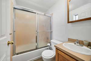 Full bath with bath / shower combo with glass door, vanity, and a textured ceiling