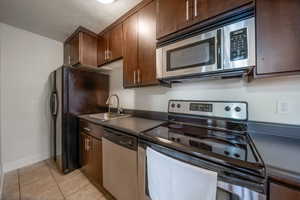 Kitchen featuring stainless steel appliances, a textured ceiling, light tile patterned floors, dark countertops, and dark brown cabinetry