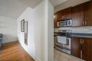 Kitchen featuring stainless steel appliances, dark brown cabinets, dark countertops, and light wood-type flooring