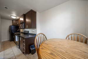 Kitchen featuring dark brown cabinets, stainless steel appliances, dark countertops, light tile patterned floors, and a textured ceiling