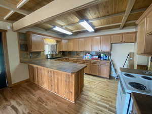 Kitchen featuring dark countertops, white electric range, light wood-style floors, a peninsula, and a wood ceiling with exposed beams
