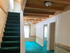 Below grade area with wainscoting, stairs, a ceiling fan, and dark carpet