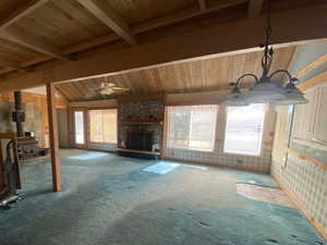 Unfurnished living room with carpet floors, a wood stove, wooden ceiling, and a stone fireplace