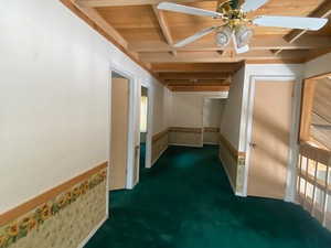 Empty room with a wainscoted wall, beamed ceiling, dark colored carpet, and a ceiling fan