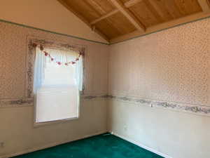 Empty room featuring vaulted ceiling, dark carpet, and wooden ceiling