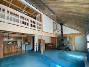 Unfurnished living room featuring ceiling fan, a wood stove, wood walls, concrete floors, and high vaulted ceiling