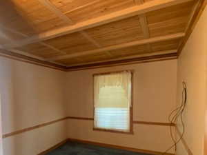 Unfurnished room featuring dark colored carpet and wooden ceiling