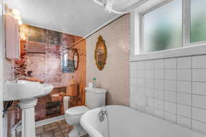 Full bath with tile walls, a freestanding bath, and a textured ceiling