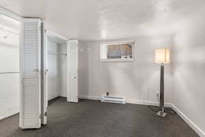 Unfurnished bedroom with a textured ceiling, dark carpet, baseboard heating, and a closet