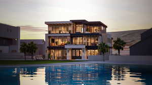 Back of property at dusk featuring a balcony, a patio, a community pool, and stucco siding