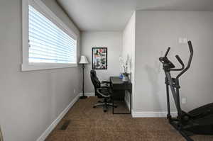Home office with dark colored carpet and baseboards