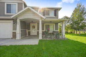 View of front facade featuring a porch, stone siding, a front lawn, a garage, and board and batten siding