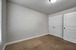 Unfurnished bedroom featuring dark colored carpet, a closet, and a textured ceiling