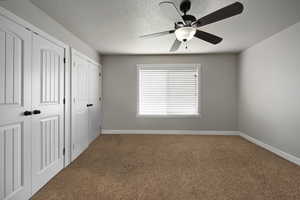 Unfurnished bedroom featuring multiple closets, carpet flooring, a textured ceiling, and ceiling fan