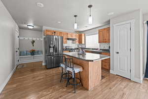 Kitchen with backsplash, hanging light fixtures, stainless steel appliances, a center island, and a breakfast bar area