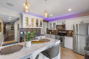 Kitchen featuring stainless steel appliances, dark stone countertops, decorative backsplash, white cabinetry, and recessed lighting