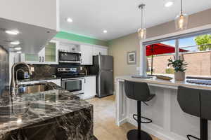 Kitchen featuring decorative backsplash, dark stone countertops, appliances with stainless steel finishes, a kitchen bar, and glass insert cabinets