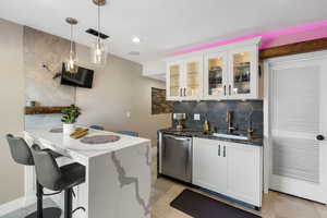 Bar area featuring tasteful backsplash, dark stone counters, pendant lighting, stainless steel dishwasher, and glass insert cabinets