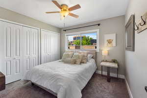 Bedroom with multiple closets, dark colored carpet, and a ceiling fan