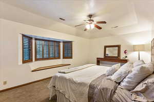 Bedroom with a textured ceiling, carpet, a ceiling fan, and a raised ceiling