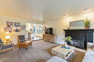Living area featuring crown molding, carpet, a fireplace with flush hearth, and a textured ceiling