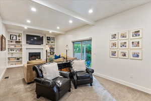 Living area featuring beamed ceiling, light colored carpet, a fireplace, recessed lighting, and built in shelves