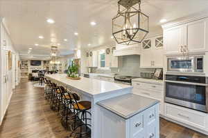Kitchen with a spacious island, stainless steel appliances, decorative light fixtures, white cabinets, and a textured ceiling