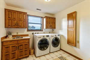Laundry room featuring cabinet space, washing machine and clothes dryer, a textured ceiling, and light floors