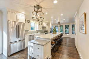 Kitchen featuring stainless steel appliances, a kitchen bar, decorative backsplash, white cabinetry, and a spacious island