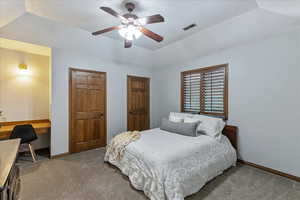 Carpeted bedroom featuring a tray ceiling, built in desk, a ceiling fan, and two closets